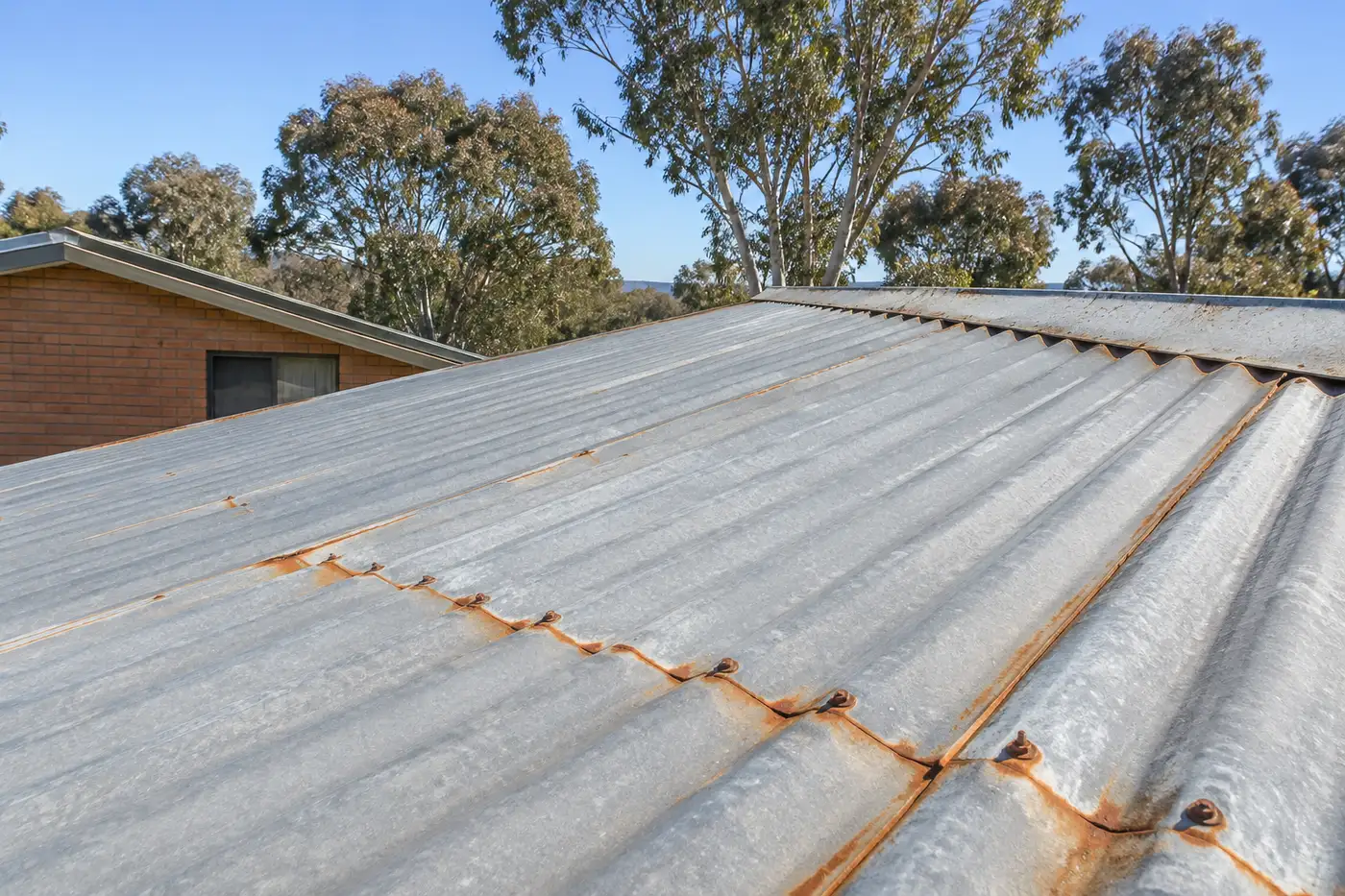 A faded Colorbond metal roof with surface rust along the sheet overlaps on a Canberra home