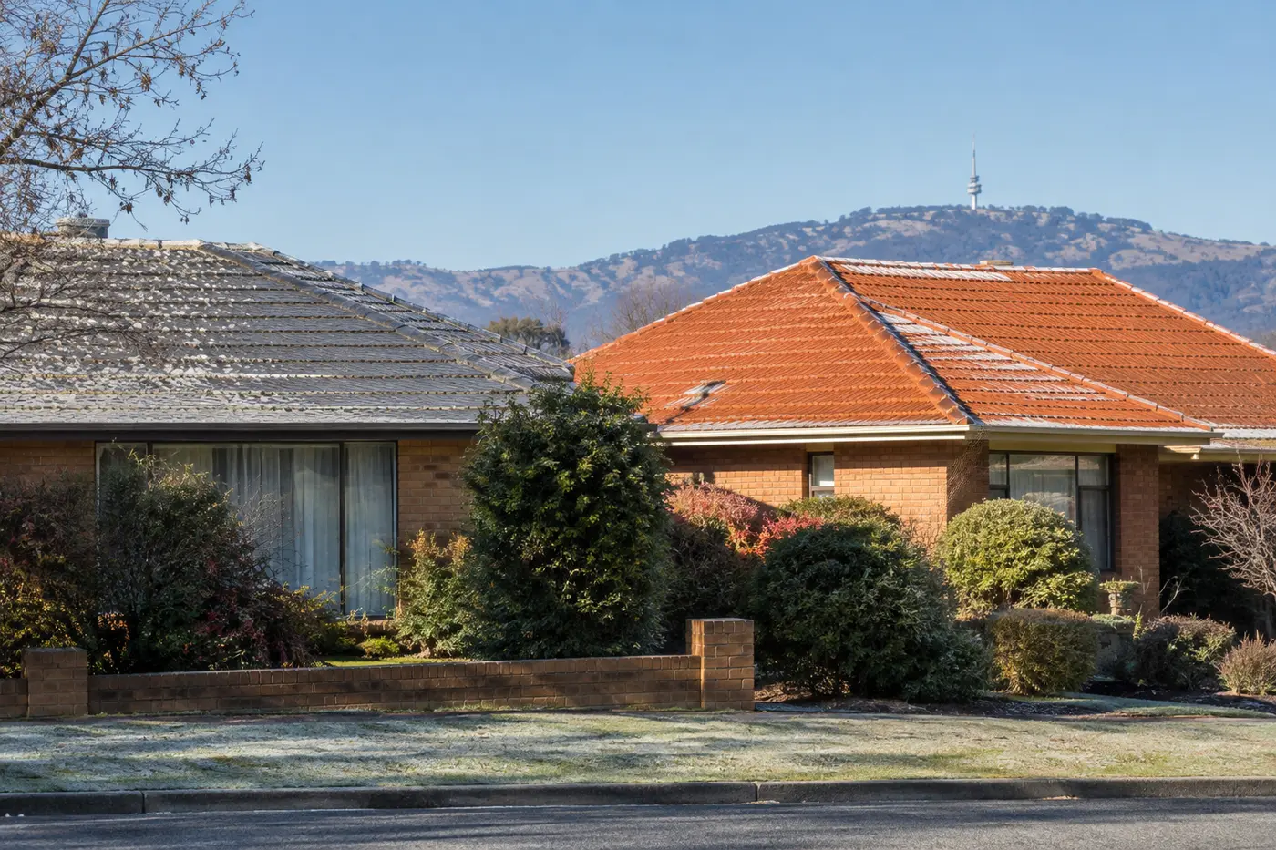 Two Canberra rooftops side by side, one with weathered grey concrete tiles and one with original orange terracotta tiles